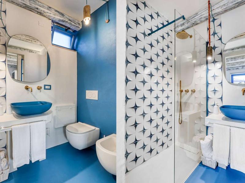 Bagno moderno con piastrelle geometriche, lavabo blu e doccia a vista.