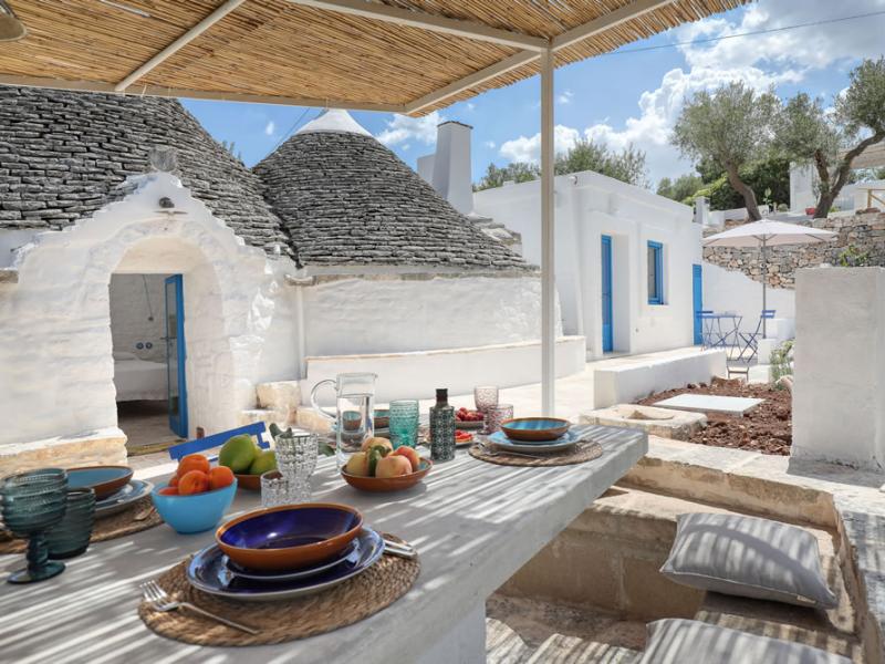 Trullo con tavolo esterno apparecchiato, tetto conico e pareti bianche.