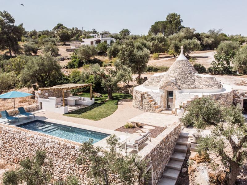 Trullo con piscina, giardino e pergolato in paesaggio rurale.