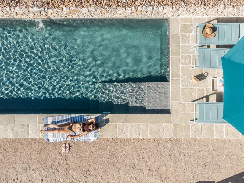 Donna prende il sole a bordo piscina con lettini e ombrellone.