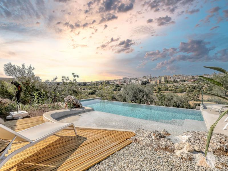 Piscina a sfioro con vista panoramica su una città al tramonto.