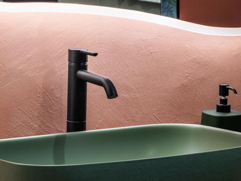 Lavabo verde con rubinetto nero e parete rosa, stile moderno.